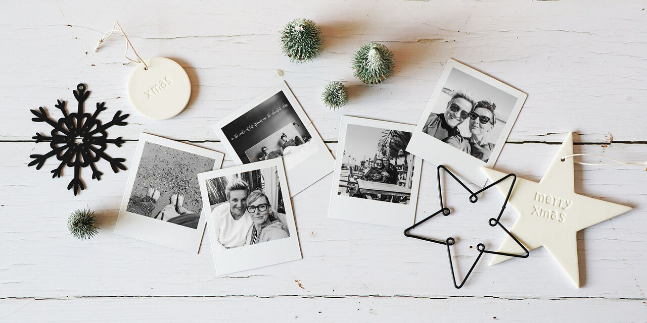 Eine kreative Anordnung von schwarz-weißen Polaroid-Fotos, die schöne Erinnerungen festhalten. Dazu dekorative Elemente wie eine Schneeflocke und kleine grüne Kugeln.