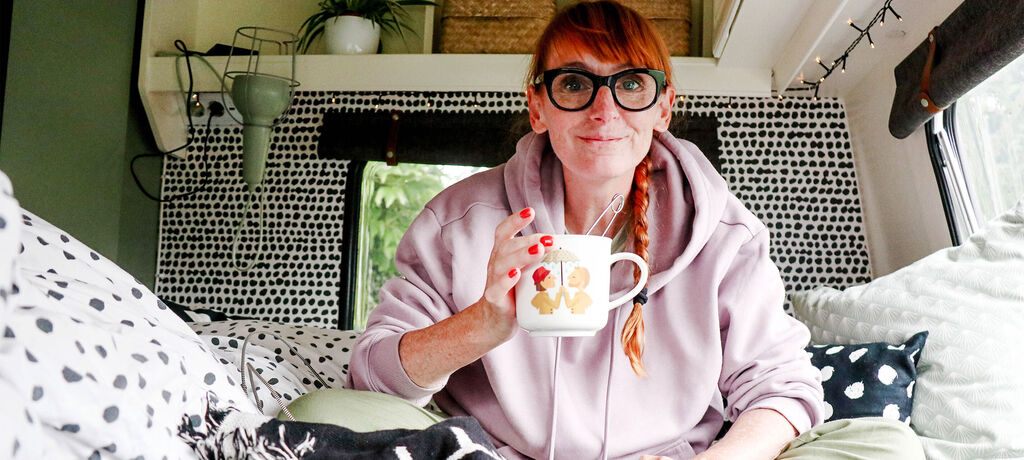 Frau in einem Van genießt eine Tasse Tee in einem gemütlichen Schlafzimmer mit skandinavischem Design