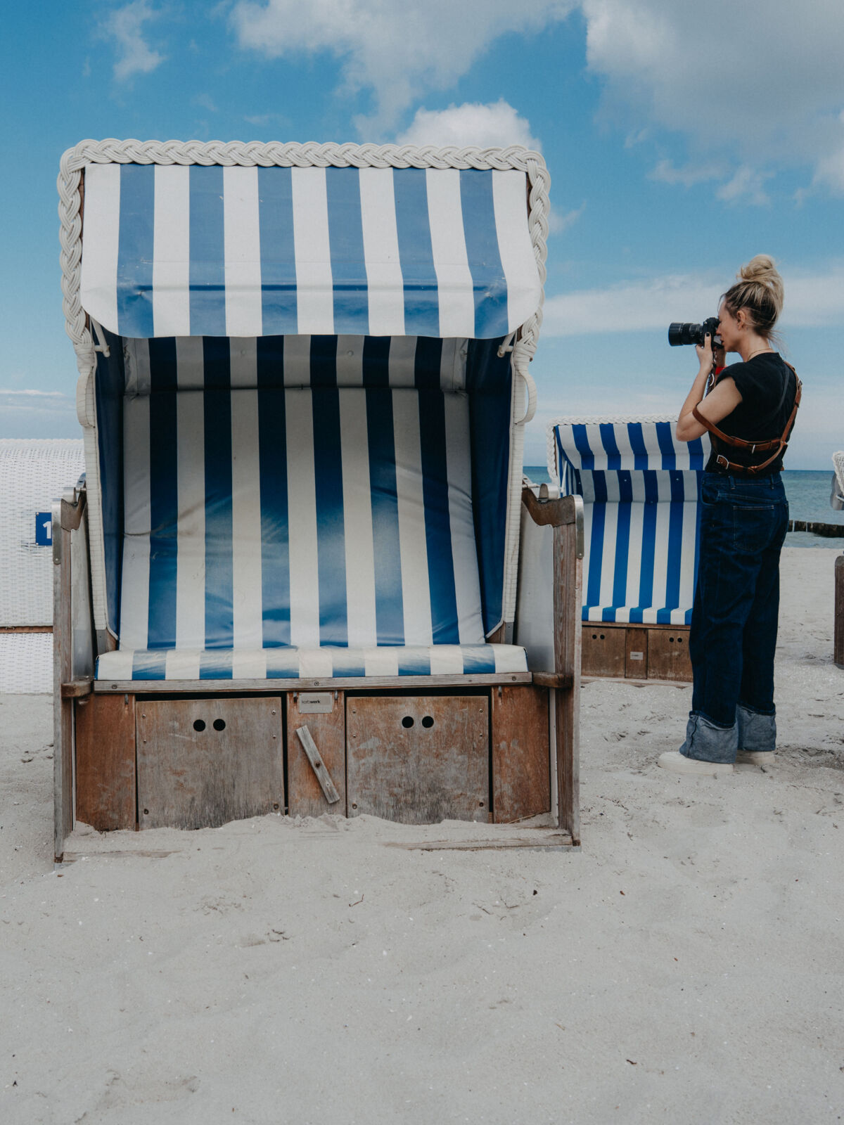 Eine Frau fotografiert zwischen Strandkörben am Strand.