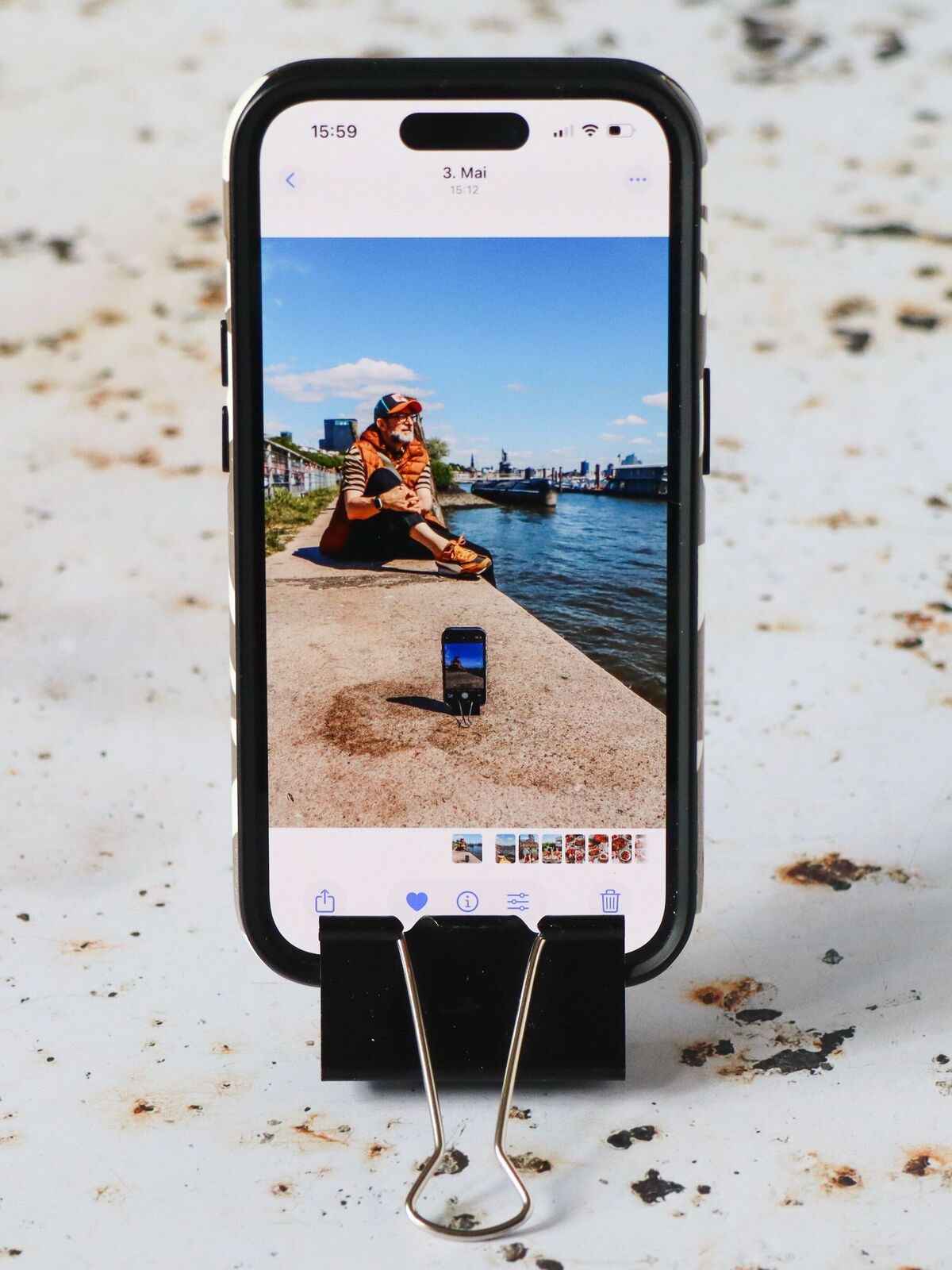 Smartphone steht aufrecht mit Klammer, darauf sieht man ein Foto von einer Person am Hafen