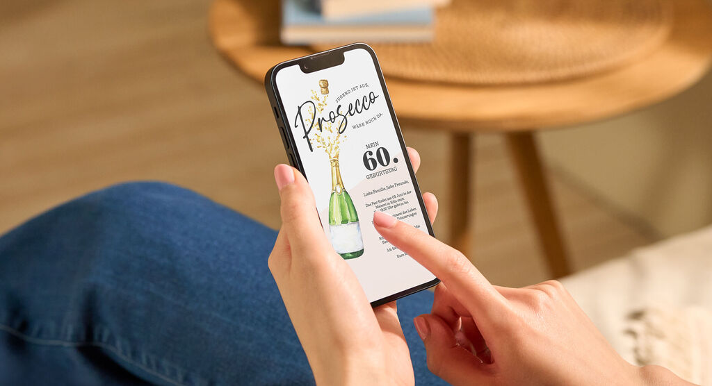 Hand hält Smartphone mit digitaler CEWE Grußkarte zum 60. Geburtstag mit Prosecco-Flasche