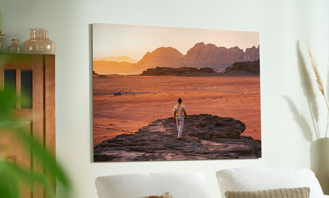 Ein Mensch steht im Licht der Abendsonne in einer weiten, roten Wüstenlandschaft mit Bergen im Hintergrund