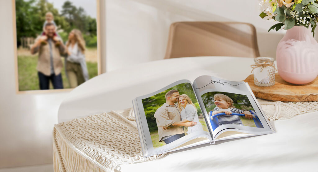 Ein offenes CEWE FOTOBUCH liegt auf einem Tisch, im Hintergrund sieht man zwei Menschen vor einer Naturkulisse.