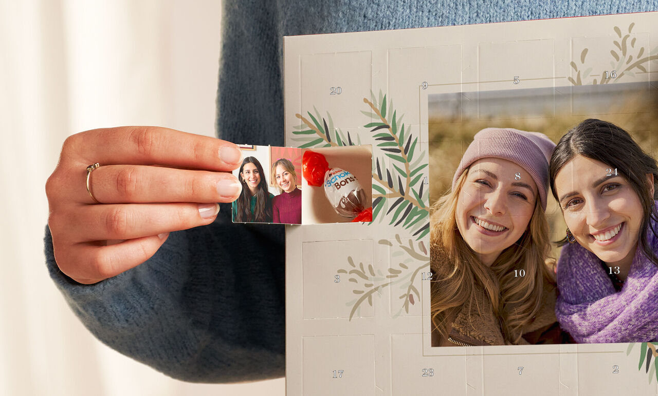 Händchen hält ein Kinderfoto und eine Schokolade vor einem adventlichen Wandbild