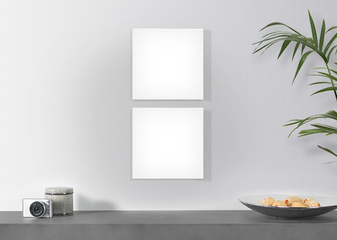 Zwei leere quadratische Wandbilder auf grauer Wand, daneben eine Kamera und eine Schüssel mit Snacks