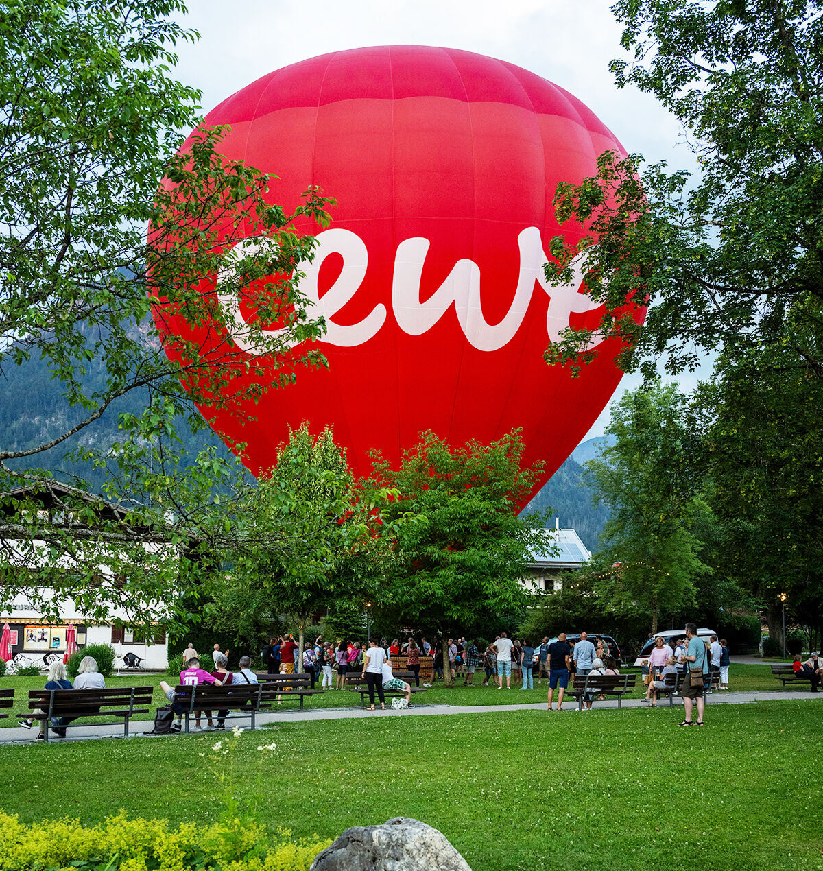 Im Vordergrund ist eine grüne Wiese. Im Hintergrund sieht man einen großen roten Heißluftballon mit CEWE Schriftzug.