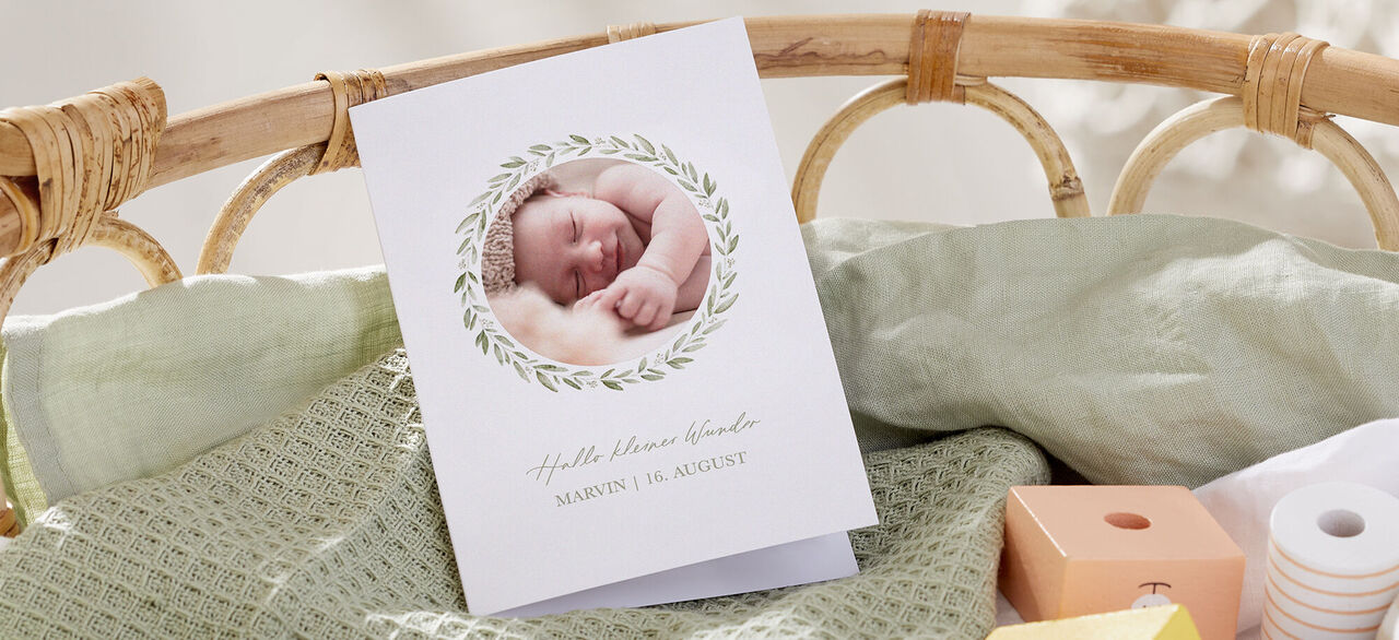 Eine liebevolle Grußkarte mit einem schlafenden Baby und einem runden Blumenkranz. Die Karte zeigt den Text 'Hallo Marvin, Willkommen' und das Datum.