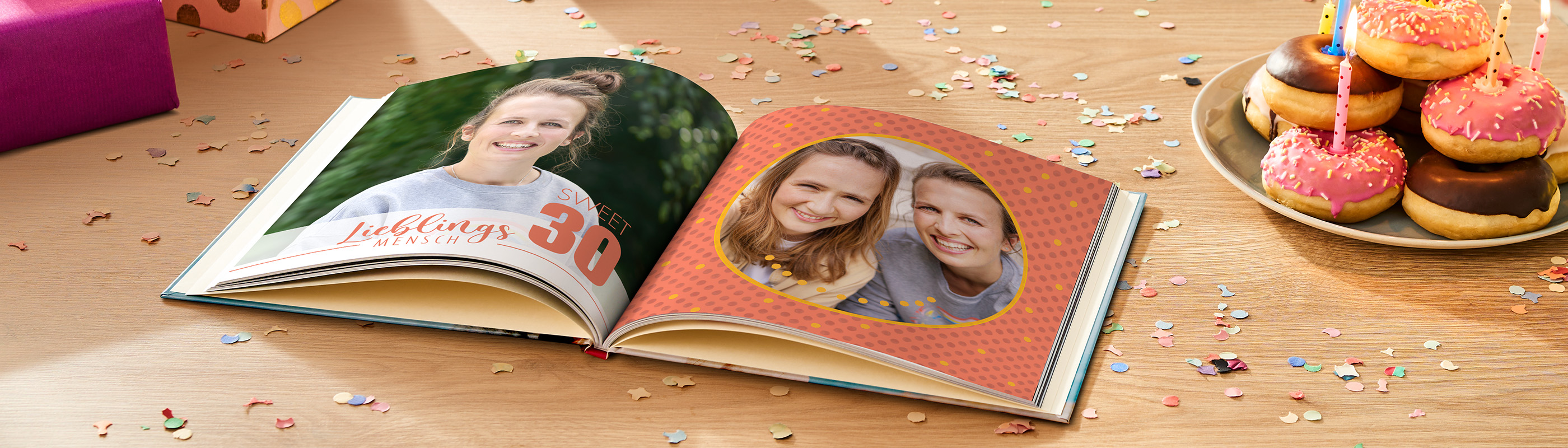 Ein CEWE FOTOBUCH liegt auf einem Tisch, umgeben von bunten Geschenken und Konfetti