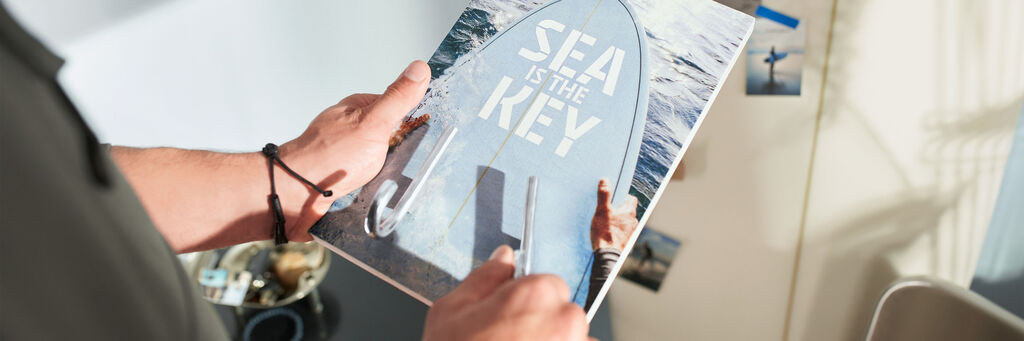 Ein enthusiastischer Mensch hält ein Fotobuch mit maritimem Cover in den Händen und zeigt darauf. Der Text lautet: "Sea is the Key".