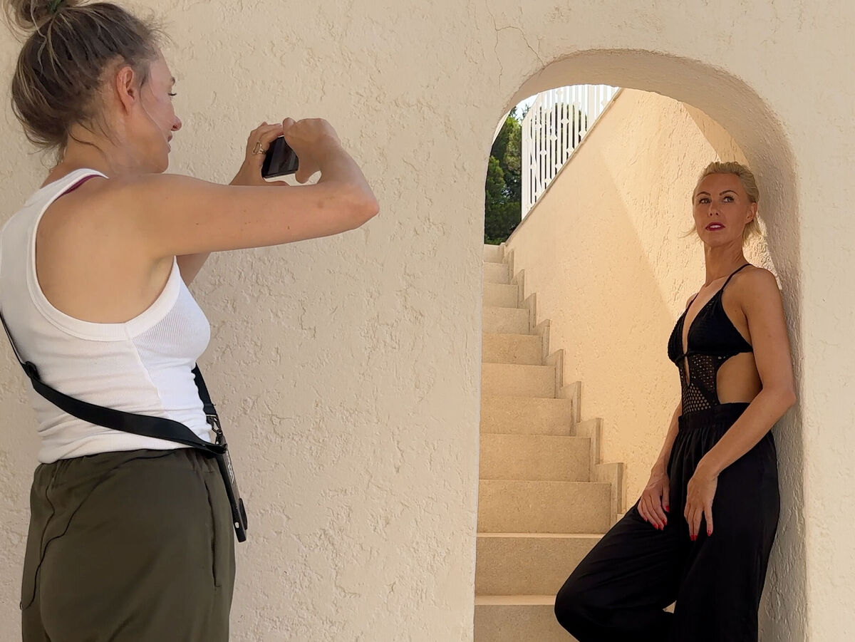 Eine Frau posiert auf einer Treppe, während eine andere Frau sie fotografiert.