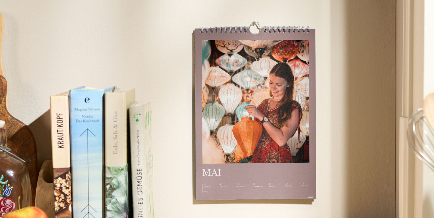 CEWE Fotokalender hängt an der Wand, zeigt den Monat Mai mit Foto einer Person vor bunten Lampions