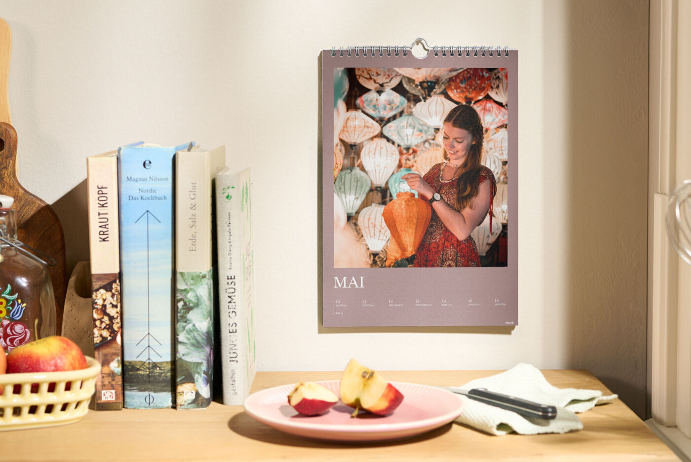 CEWE Fotokalender hängt an der Wand, zeigt den Monat Mai mit Foto einer Person vor bunten Lampions