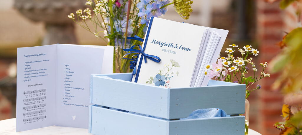 Eine liebevoll gestaltete Einladungskarte in einem Holzkasten, umgeben von frischen Blumen