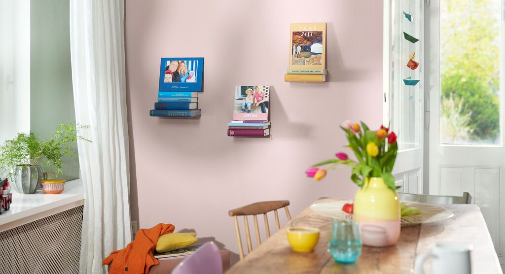Bücher und Fotos auf Regalen an einer Wand, mit fröhlichen Blumen auf einem Tisch.