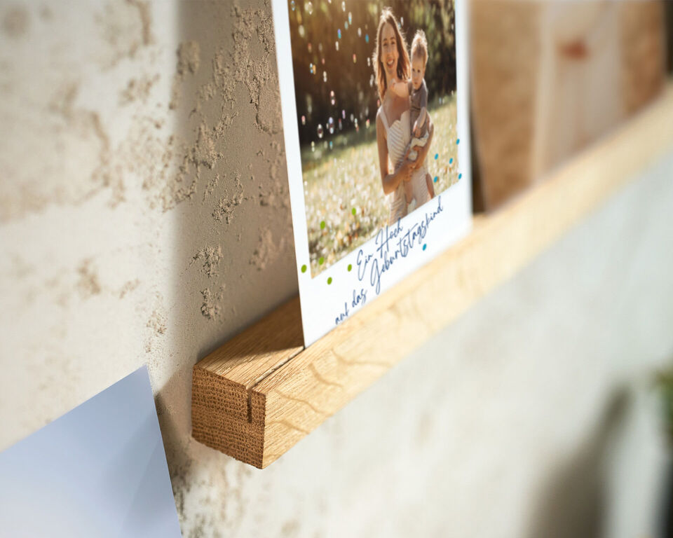 Foto mit handschriftlicher Notiz steht auf einer Holzleiste an einer hellen Wand