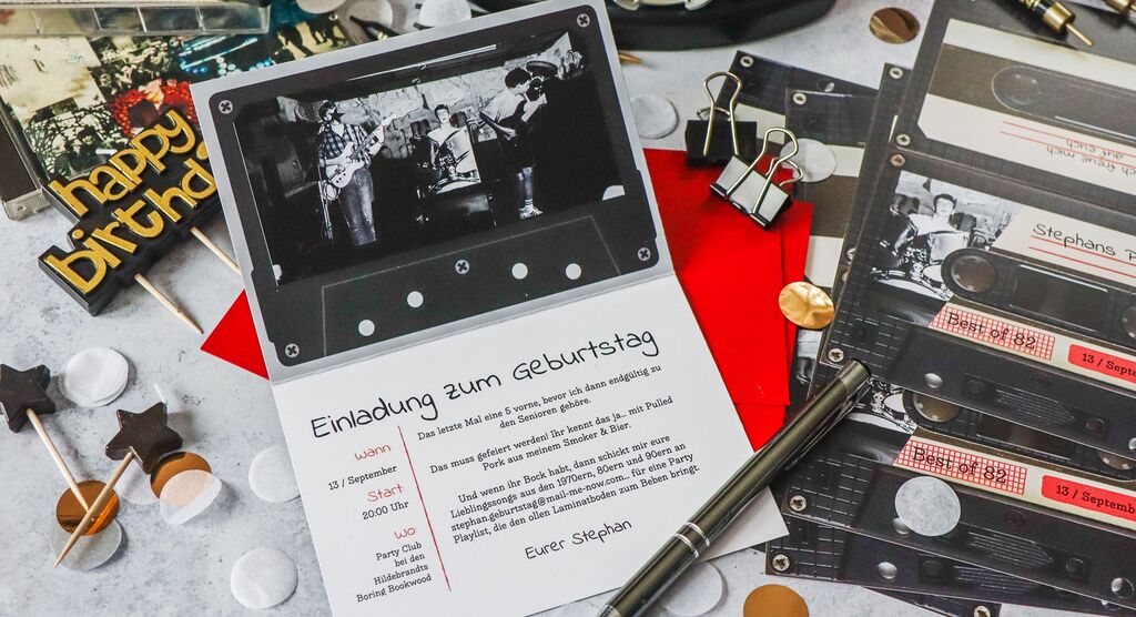 Geburtstagseinladungskarte mit Schwarz-Weiß-Foto und Text umgeben von weiteren Karten im Kassetten-Design, Stift, Mini-Drumset und Konfetti.