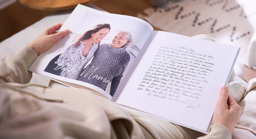 Eine Frau hält in ihren Händen ein aufgeschlagenes CEWE FOTOBUCH, das ein großes Foto und einen eingescannten Brief zeigt.