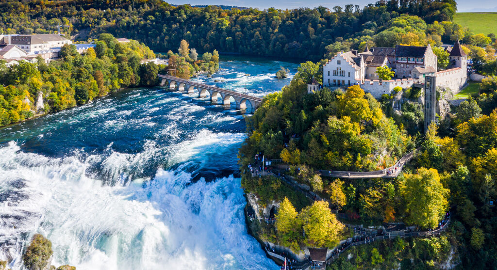 Atemberaubender Blick auf den Rheinfall mit herbstlichen Bäumen und historischer Architektur im Hintergrund.
