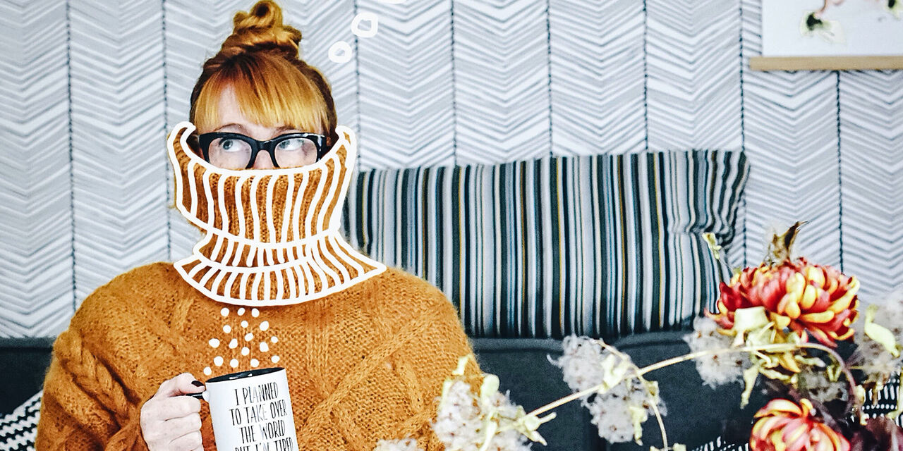 Eine Person in einem gemütlichen Pullover hält eine Tasse, umgeben von Blumen und einer stilvollen Couch.