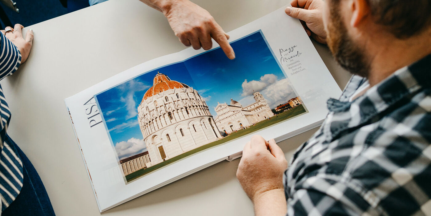 Zwei Personen schauen gemeinsam in ein CEWE FOTOBUCH mit Fotos vom schiefen Turm und Baptisterium in Pisa