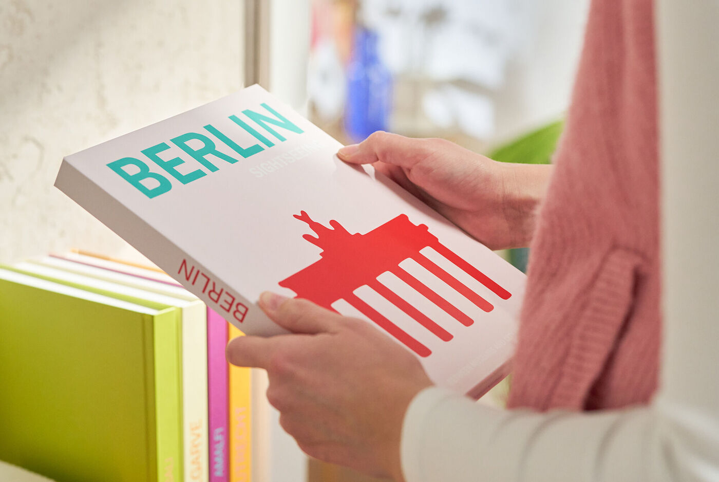 Eine Person hält ein CEWE Fotobuch über Berlin mit einem roten Brandenburger Tor.