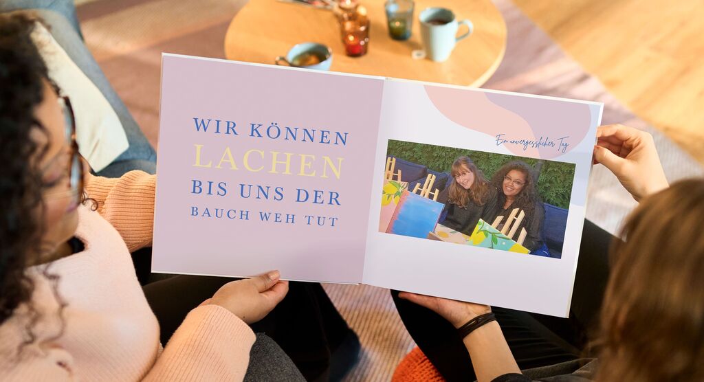 Zwei Personen lesen zusammen in einem Fotobuch mit bunten Bildern und Text.