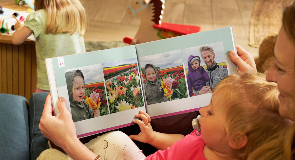 Mutter und Kind betrachten ein geöffnetes CEWE FOTOBUCH mit einer Bilderserie der Familie in einem Tulpenfeld.