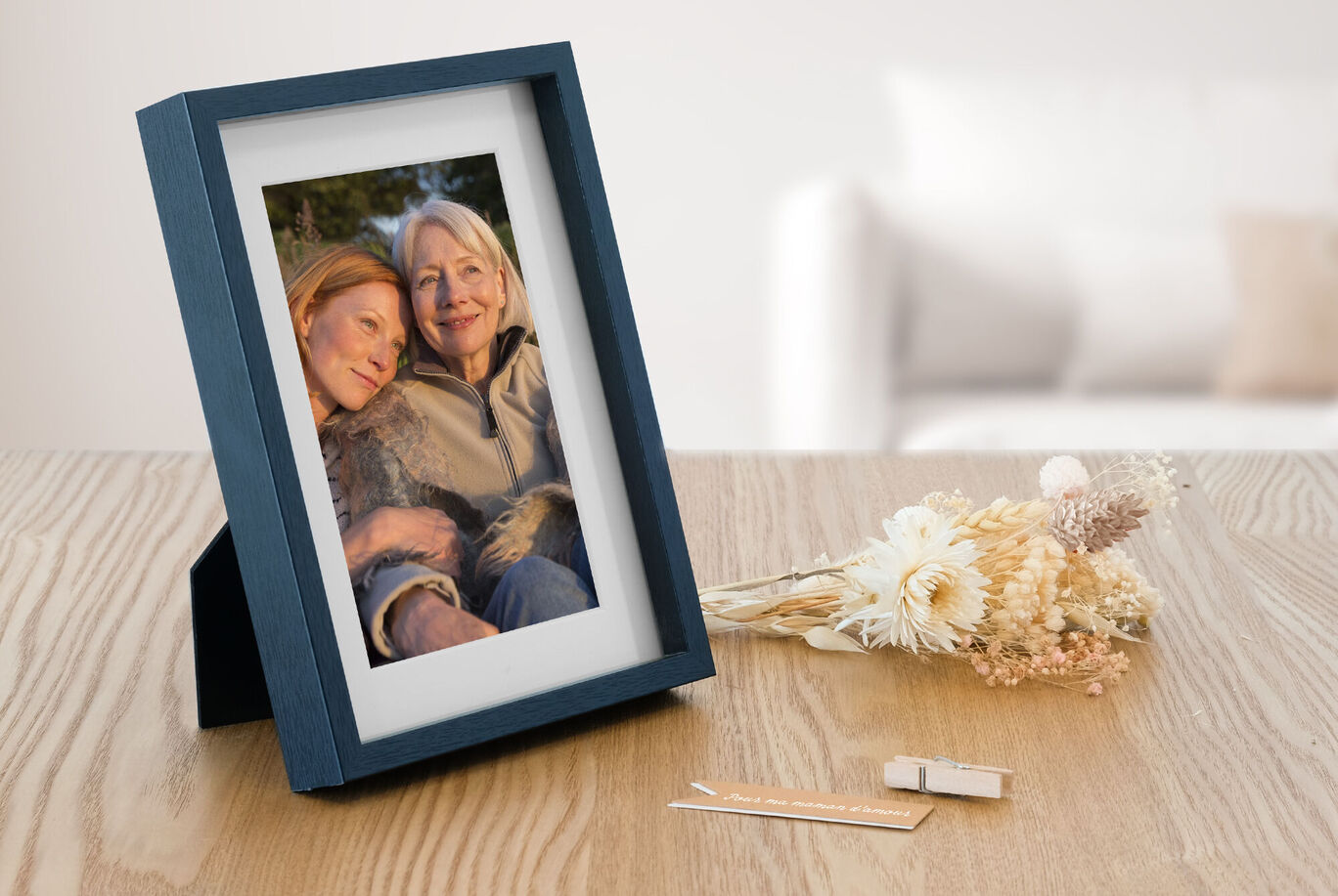 Ein liebevoll gerahmtes Foto auf einem Tisch, das schöne Momente zeigt. Daneben liegen Trockenblumen und kleine Holzstücke.
