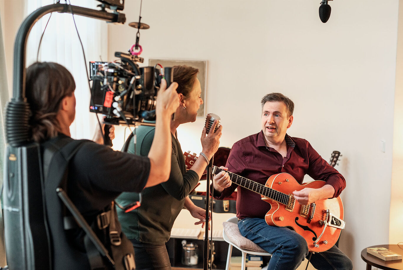 Ein Mann singt in ein Mikrofon, während ein anderer Mann Gitarre spielt, umgeben von einer freundlichen Atmosphäre.