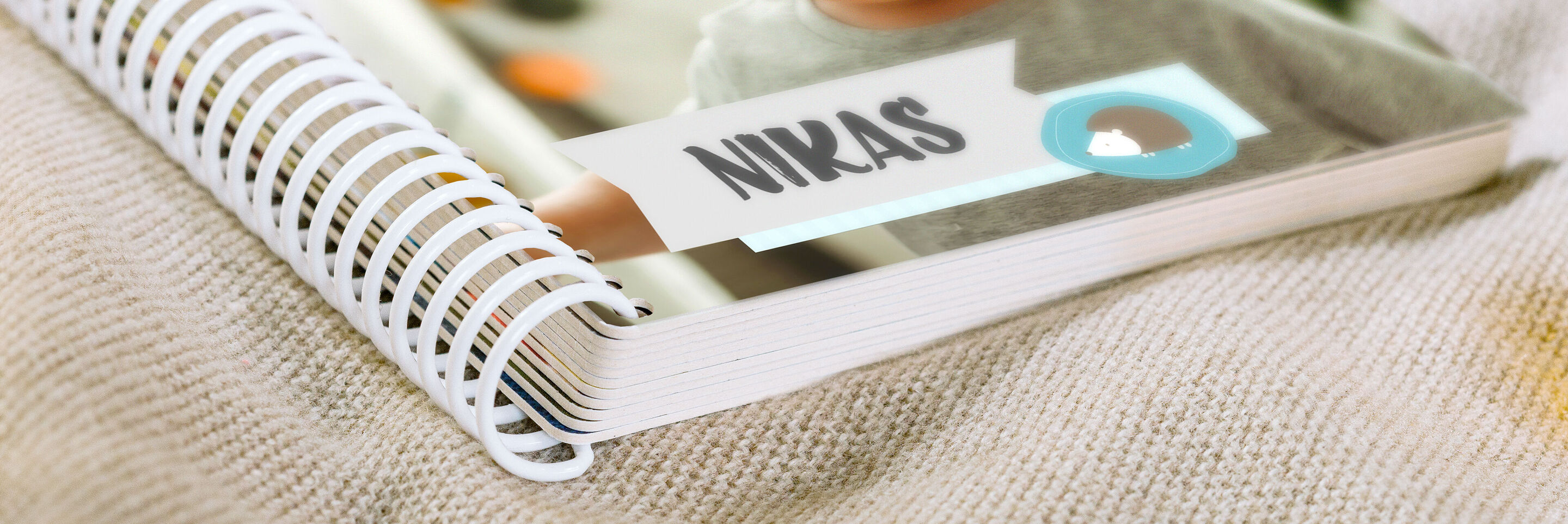 Ein offenes Fotobuch auf einem Tisch, mit dem Namen 'NIKAS' und bunten Bildern im Hintergrund, die Freude an Erinnerungen zeigen