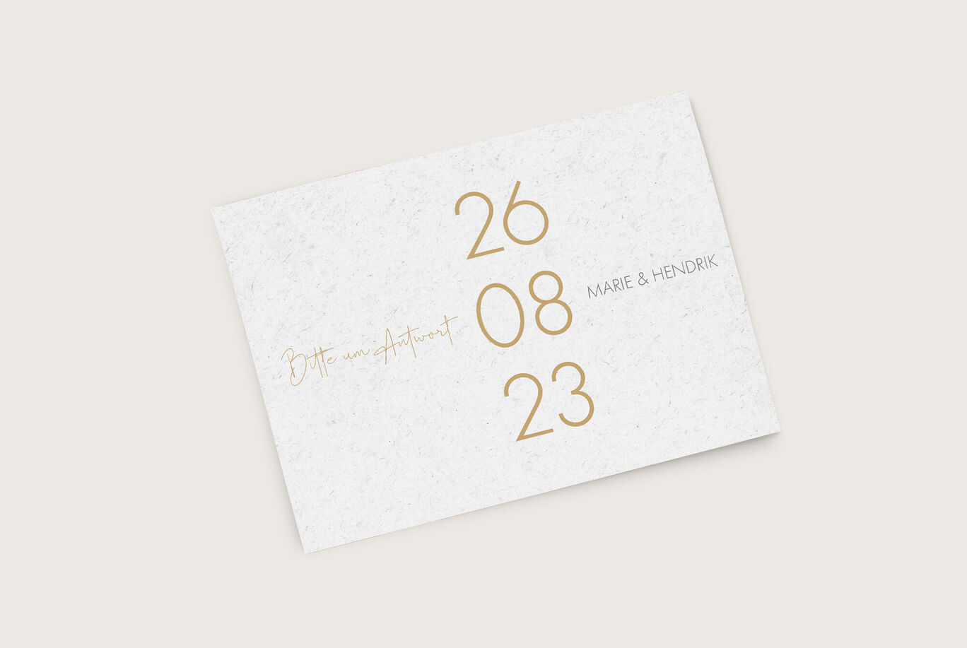 Ein elegantes Einladungskärtchen in weiß mit goldener Schrift, das den Text "Bitte um Antwort" sowie das Datum "26.08.23" und die Namen "Marie & Hendrik" präsentiert.