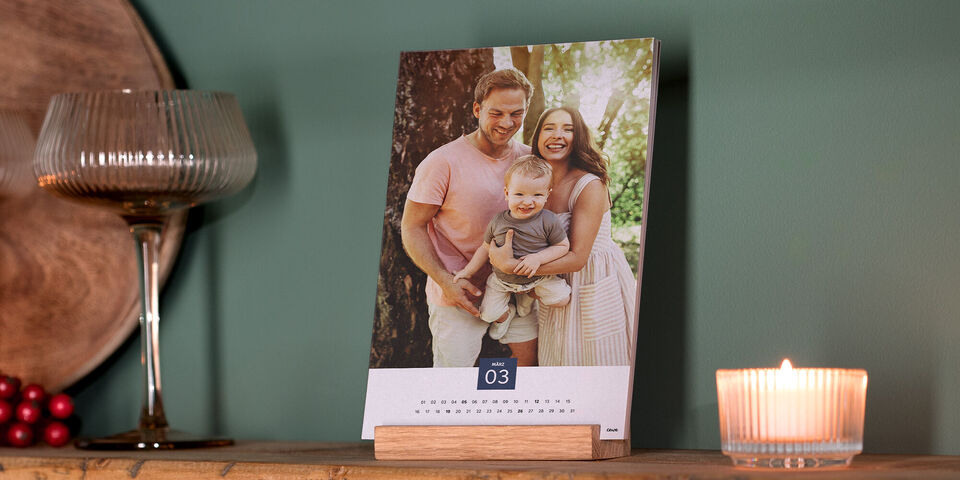 Ein kreativer Fotokalender steht auf einem Tisch, mit liebevoller Familenaufnahme im Fokus. Der Hintergrund zeigt eine dekorative Wand und Kerzenlicht.