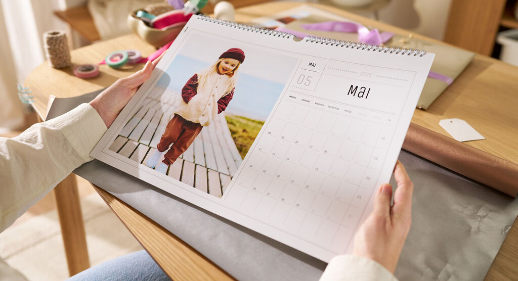 Eine Frau sitzt an einem Tisch und hält einen Wandkalender mit einem Fotomotiv von einem Kind in den Händen.