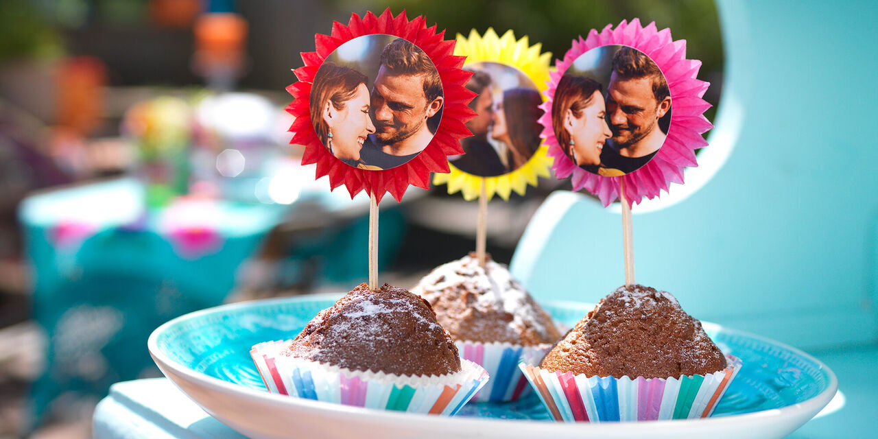 Leckere Muffins mit bunten Fotopicks auf einem Teller.