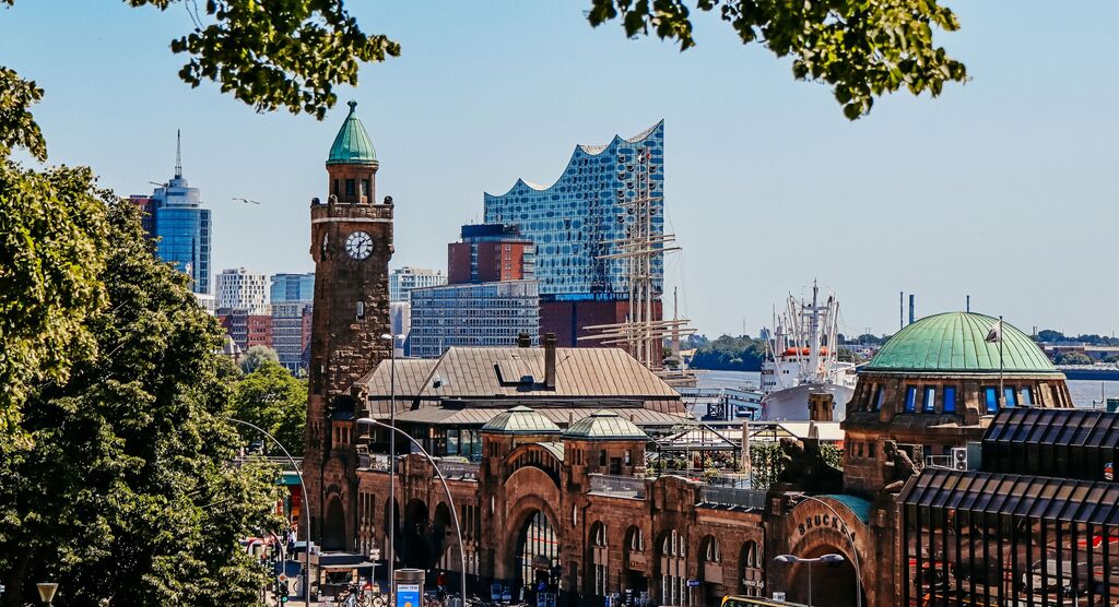 Blick auf Hamburger Hafen mit Elbphilharmonie, Sonnenschein und grünen Bäumen im Vordergrund