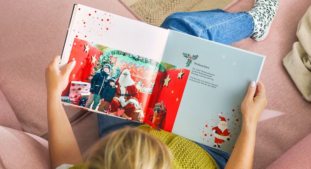Eine Person liest ein CEWE FOTOBUCH mit einem Weihnachtsmotiv und einem Santa Claus auf der Seite.