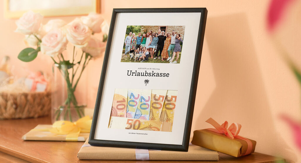 Gerahmtes Urlaubsbild mit Geldscheinen, daneben Geschenke und Rosen auf Kommode