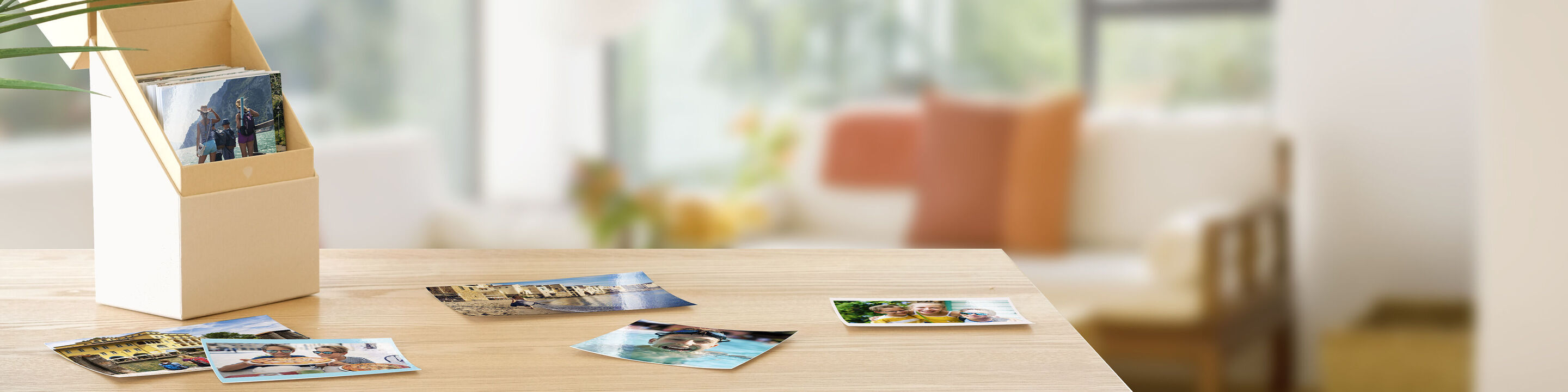 Ein Holzständer mit Fotos und Postkarten auf einem Tisch. Im Hintergrund sieht man einen Raum mit Sofa und Pflanzen.