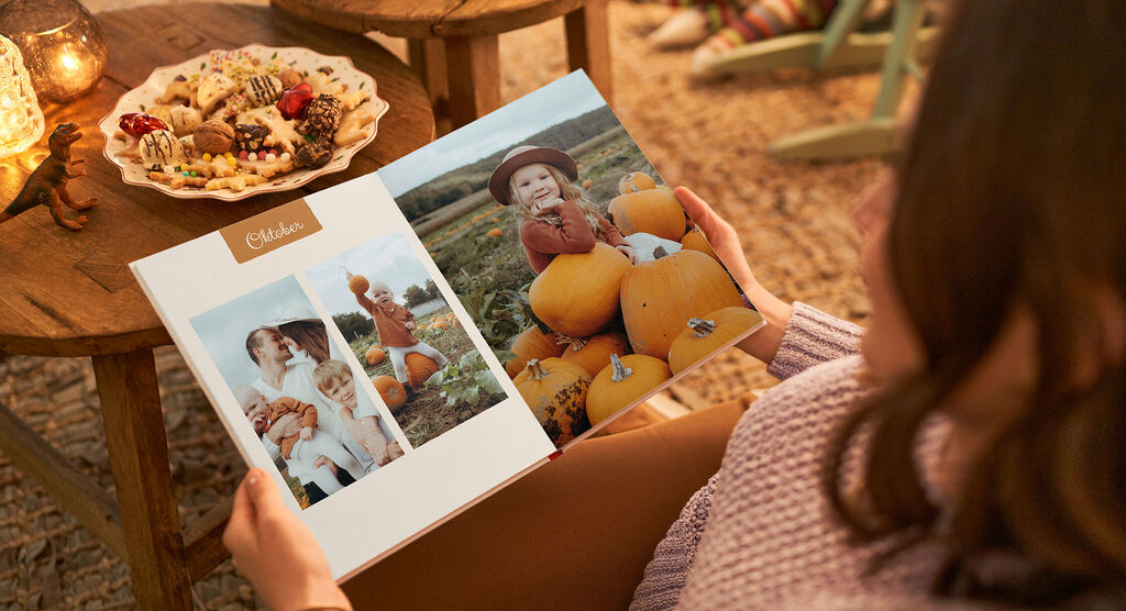 Eine Person blättert durch ein CEWE FOTOBUCH mit bunten Bildern von Freizeitaktivitäten und Kürbissen.
