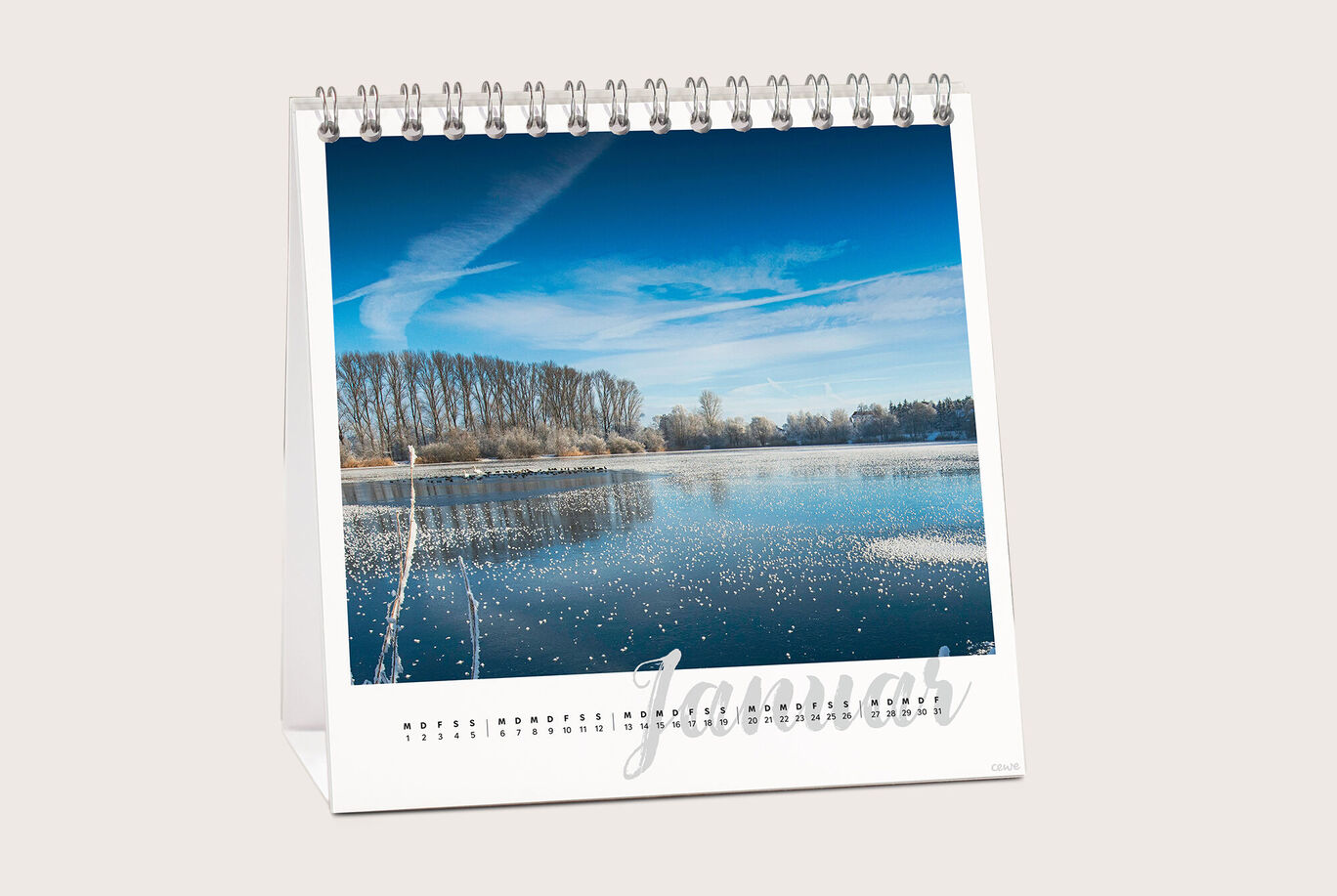 Ein schöner Fotokalender mit einem winterlichen Landschaftsbild für den Monat Januar. Der See spiegelt den klaren blauen Himmel wider.