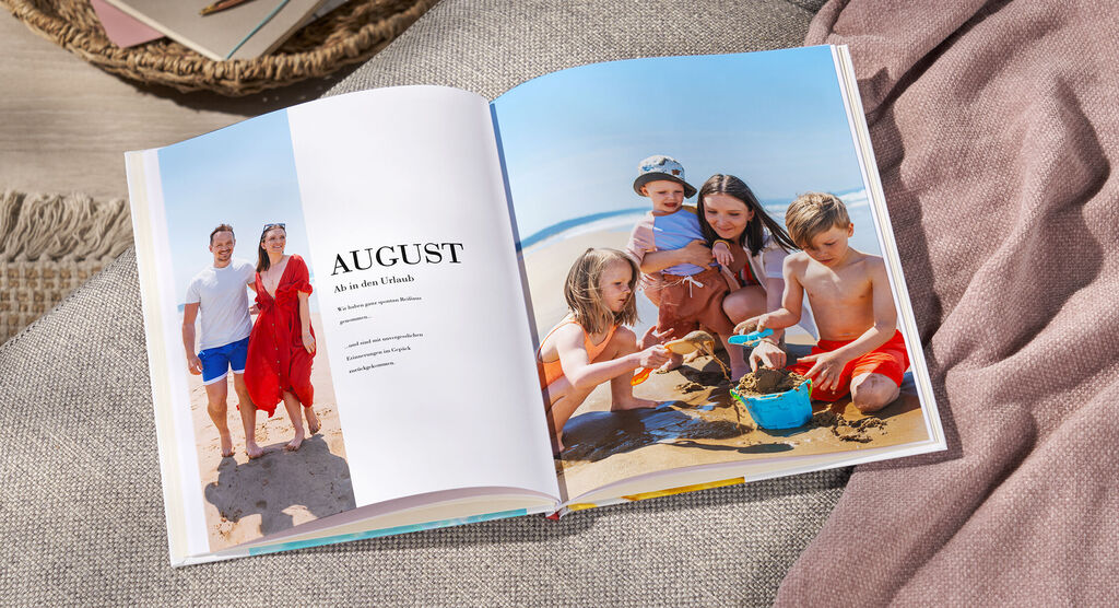 Eine offene Seite eines Fotobuchs zeigt einen Strandurlaub im August. Kinder spielen im Sand und bauen mit Förmchen.
