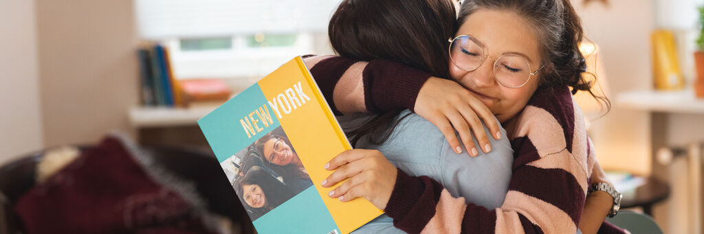 Zwei Personen umarmen sich und halten ein CEWE FOTOBUCH mit Bildern von New York.