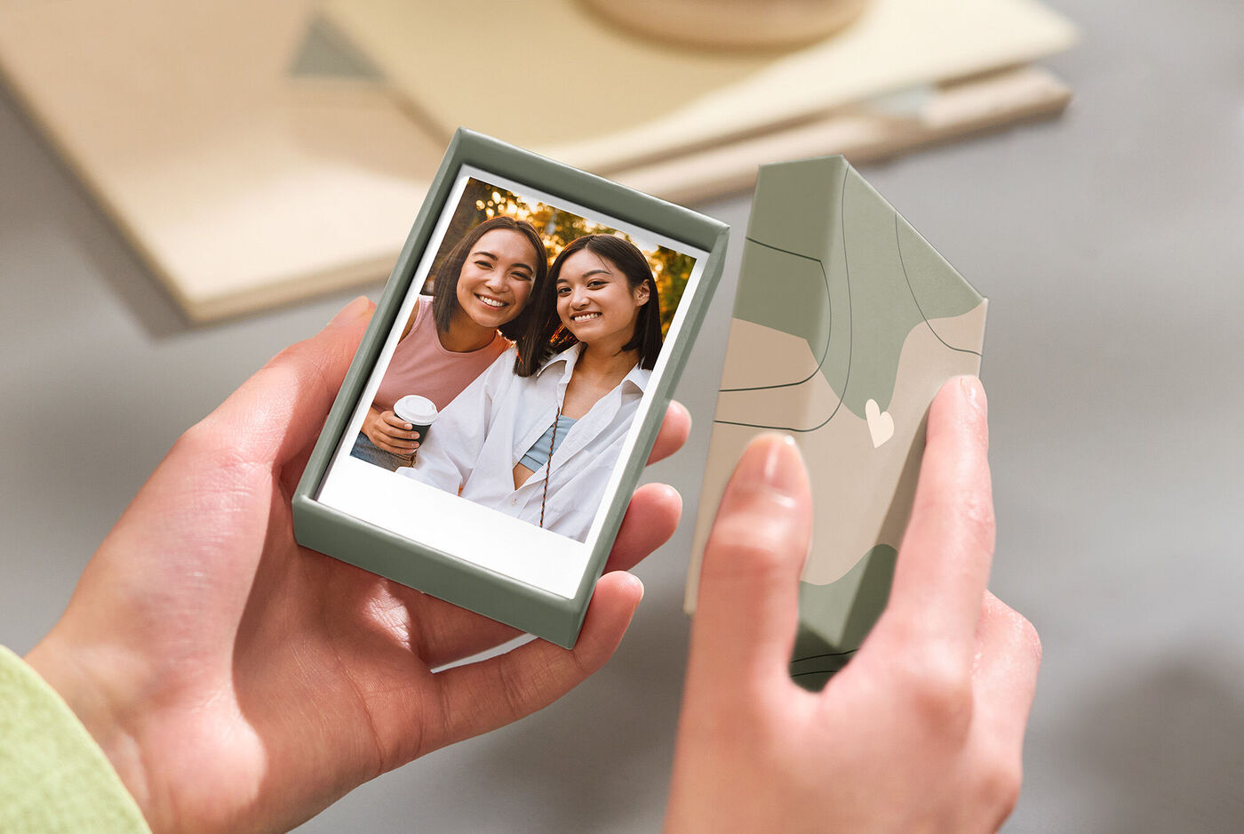 Eine Person hält eine wunderschöne, personalisierte Box mit einem Foto in der Hand. Die Box ist hellgrün und hat ein ansprechendes Design. Im Hintergrund sind andere Materialien zu sehen, die kreatives Gestalten anregen.