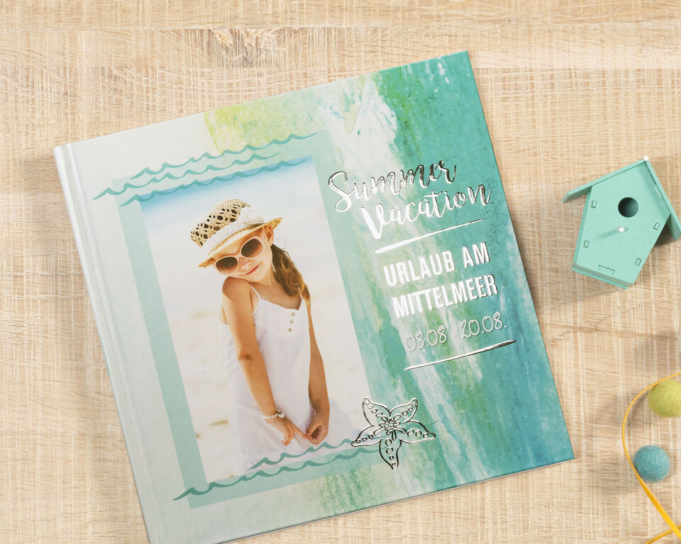 Ein schönes CEWE FOTOBUCH mit einem sommerlichen Cover in sanften Farben, das Urlaubserinnerungen zeigt