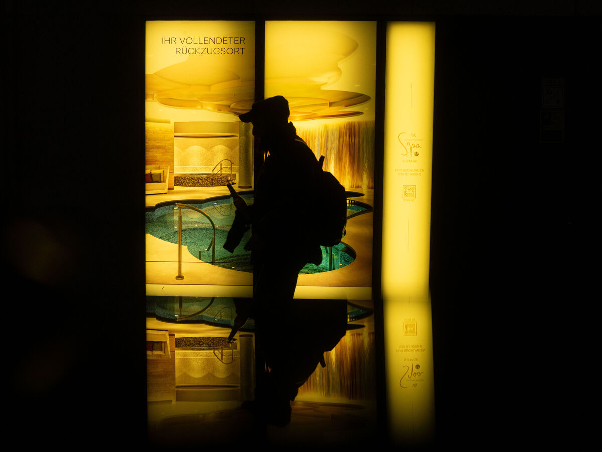 Dunkle Silhouette einer Person vor warm gelb leuchtenden Fenstern mit Spiegelung auf dem Boden