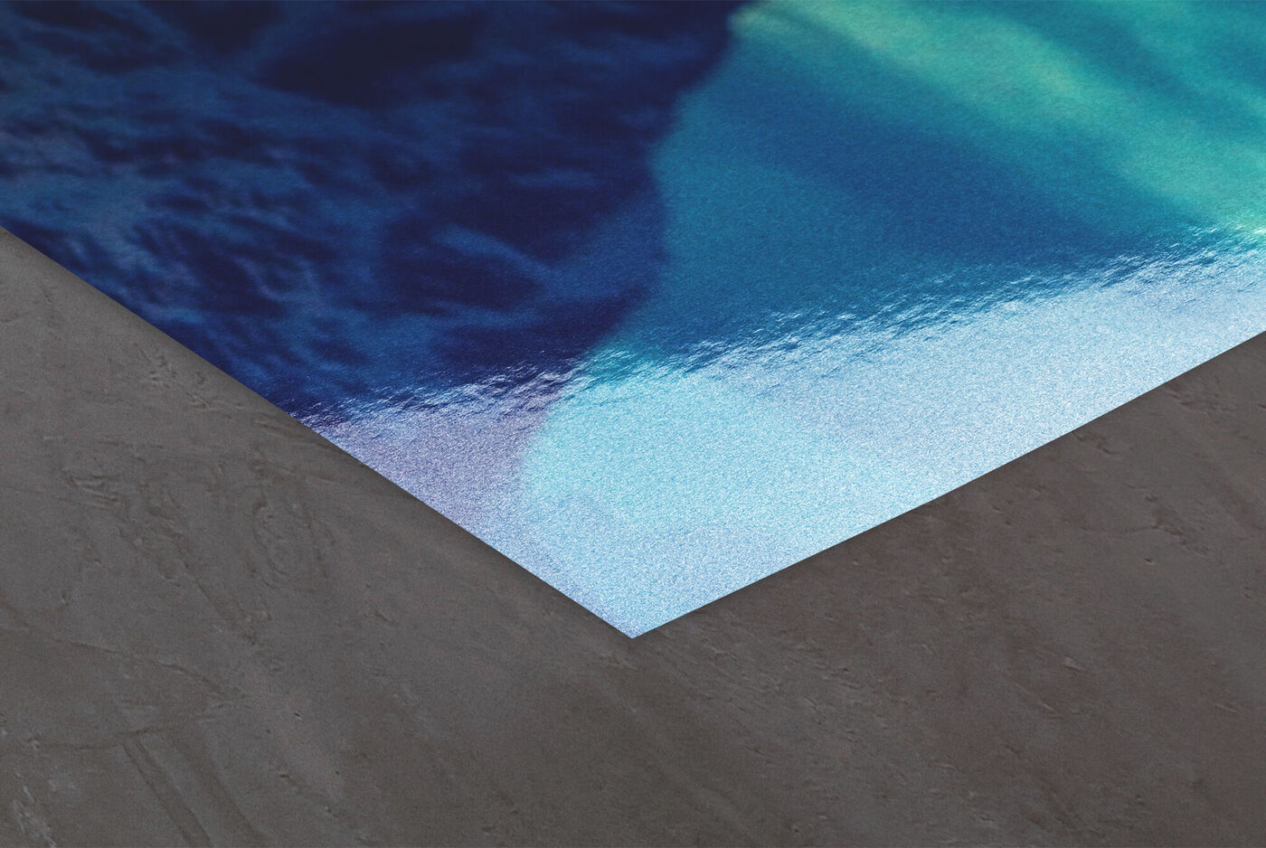 Ecke eines CEWE Posters mit glänzendem blauen Bildmotiv auf grauem Untergrund