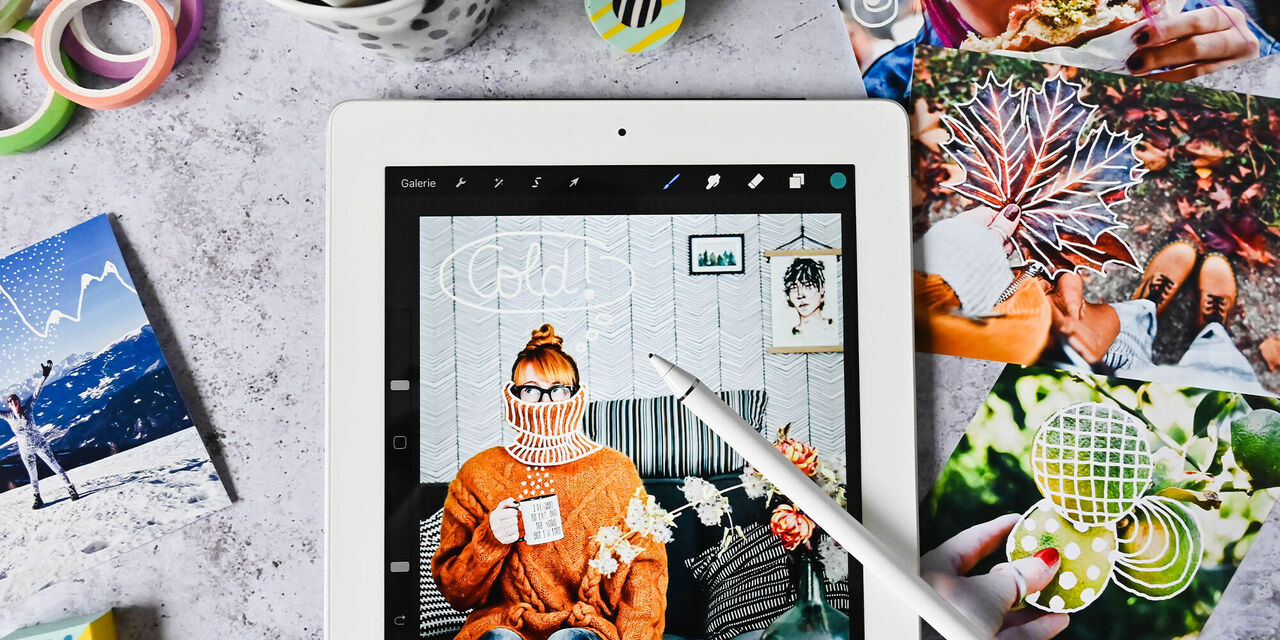 Eine Person bearbeitet Fotos auf einem Tablet. Darauf sind kreative Designs zu sehen. Rundherum liegen verschiedene Fotokarten und Dekorationen.