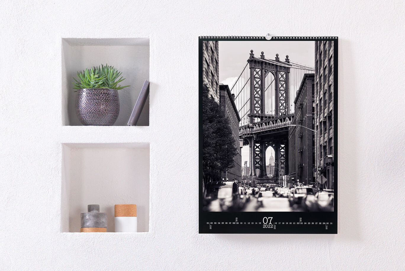 Wunderschöner Wandkalender mit einer schwarz-weiß Aufnahme der Brooklyn Bridge in New York, umgeben von einer modernen Wand mit Pflanzen und Dekor.