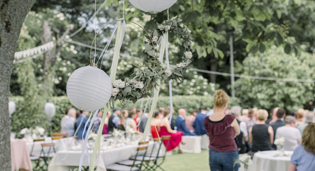 Hochzeitsfeier im Garten mit dekorativen Laternen und Blumenkranz