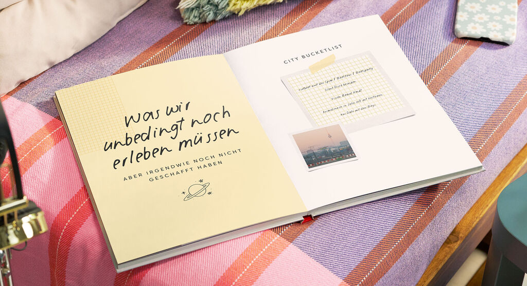 Auf einem bunten Sofa liegt ein aufgeschlagenes CEWE FOTOBUCH. Darin ist eine Liste mit mehreren Punkten zu sehen.
